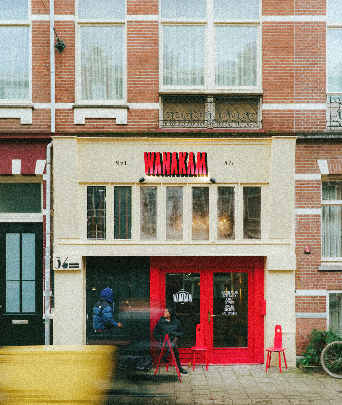 Wanakam café shopfront at number 34, with its red sign, doors and chairs.
